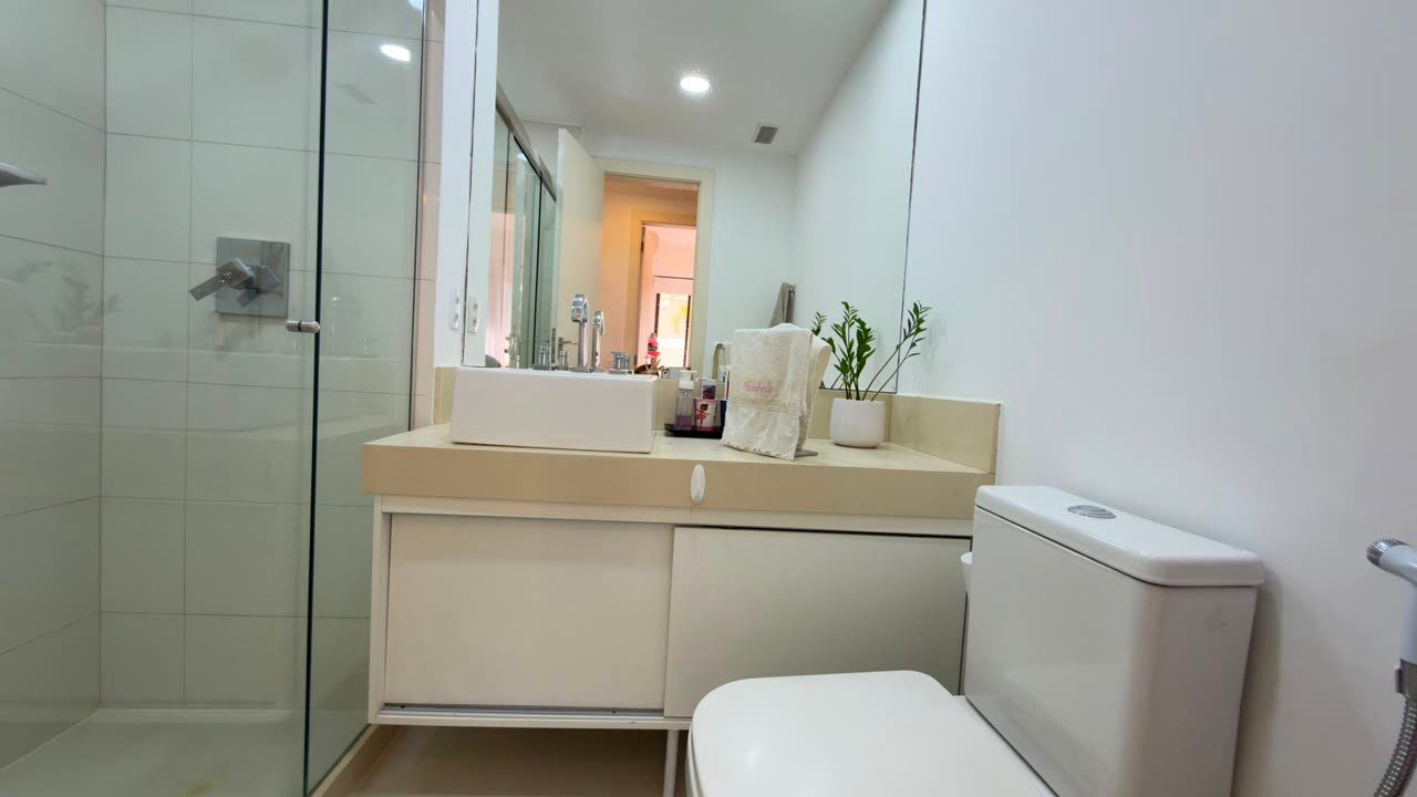Banheiro com box de vidro, bancada e espelho amplo no apartamento reformado