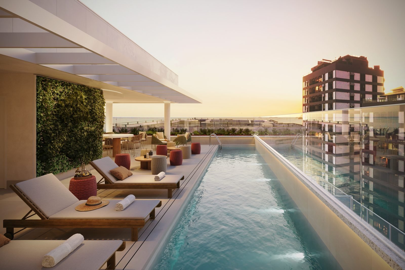 Piscina do rooftop do Be.in.Rio Praia Ipanema ao pôr do sol, com espreguiçadeiras e jardim vertical