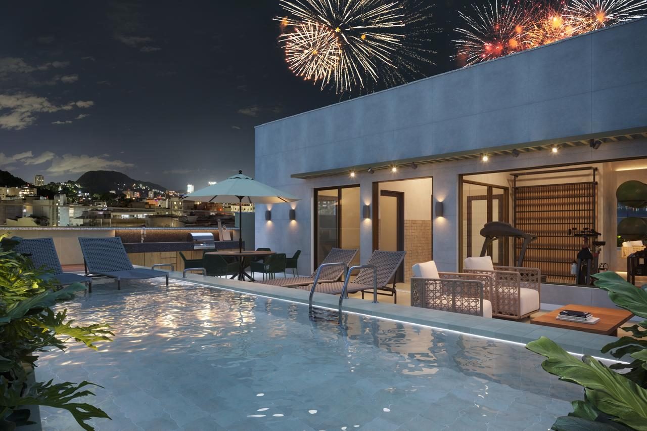 Piscina do rooftop do Be.in.Rio Tonelero à noite, com fogos de artifício sobre Copacabana ao fundo