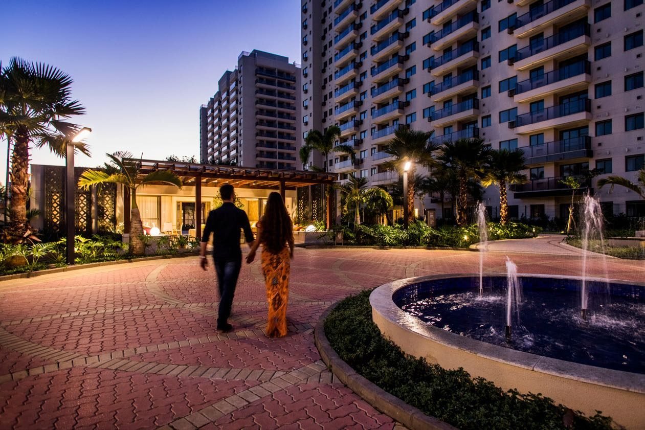 Alameda arborizada do Like Residencial Club à noite, com espelho d'água iluminado