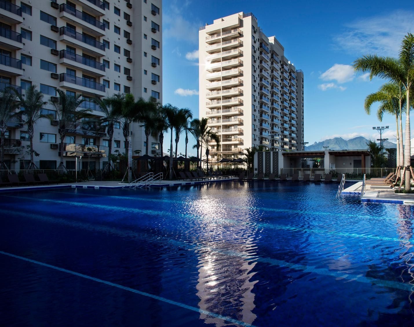 Piscina de raia de 25 metros do Like Residencial Club, com deck e as fachadas ao fundo